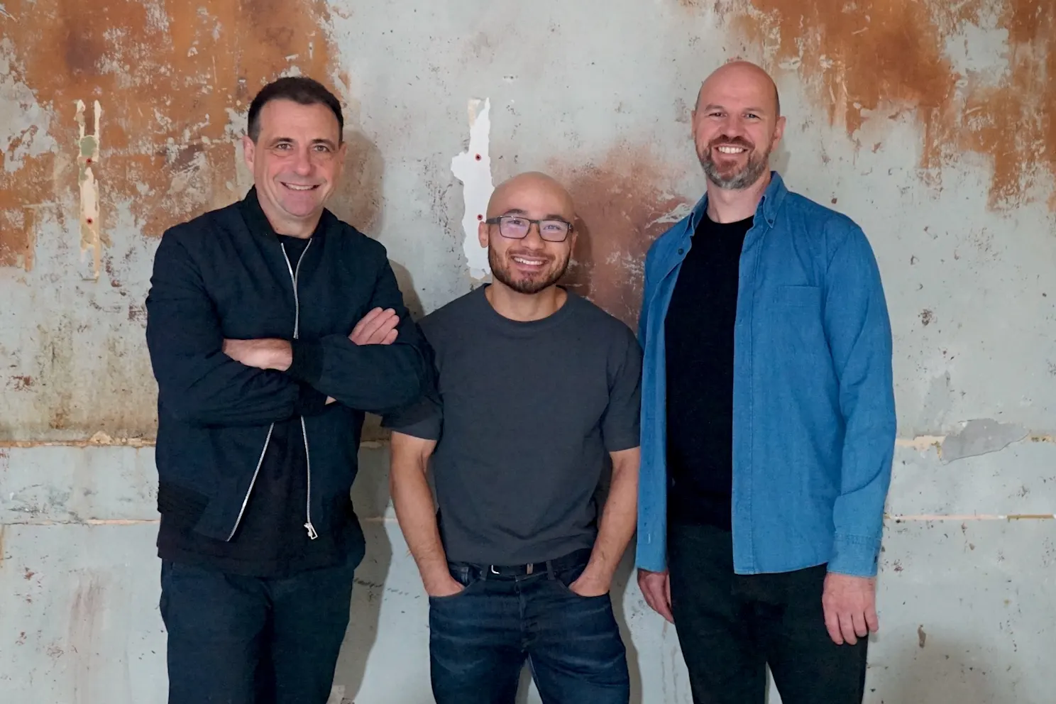 Chef Khanh Nguyen (center) smiling with two colleagues against a weathered wall